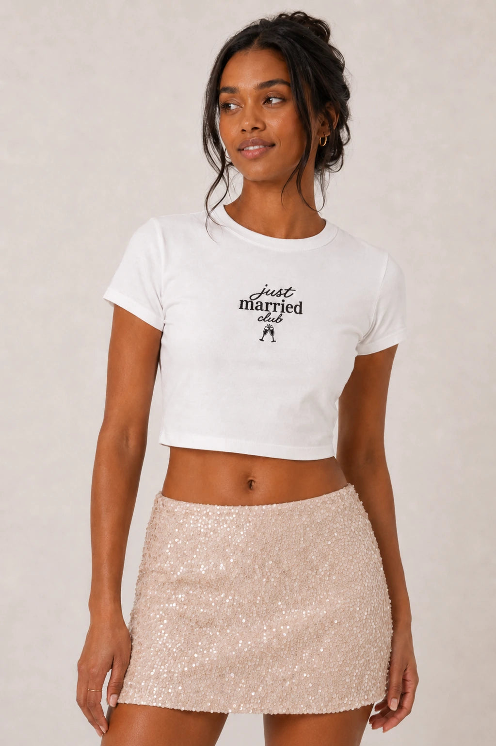 Woman wearing a white 'just married club' t-shirt and beige sequin skirt on a plain background