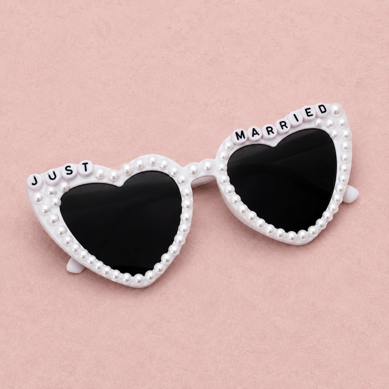 Heart-shaped sunglasses with 'Just Married' text on a pink background