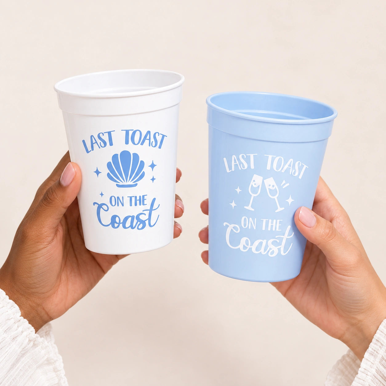 Two hands hold a white and a light blue plastic cup with matching lids, both printed with the phrase 'LAST TOAST ON THE Coast' and decorative coastal-themed graphics.