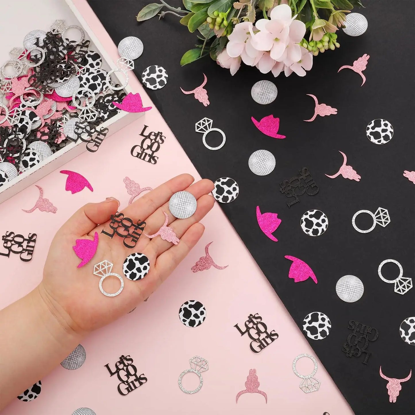 Hand holding confetti with 'Let's Go Girls' design on a pink and black background with floral decorations.