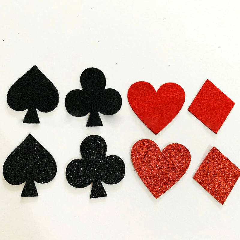 Six playing card suit confetti on a white background, including four black spades and clubs and two red hearts and diamonds, with one matte black and one glittery red finish.