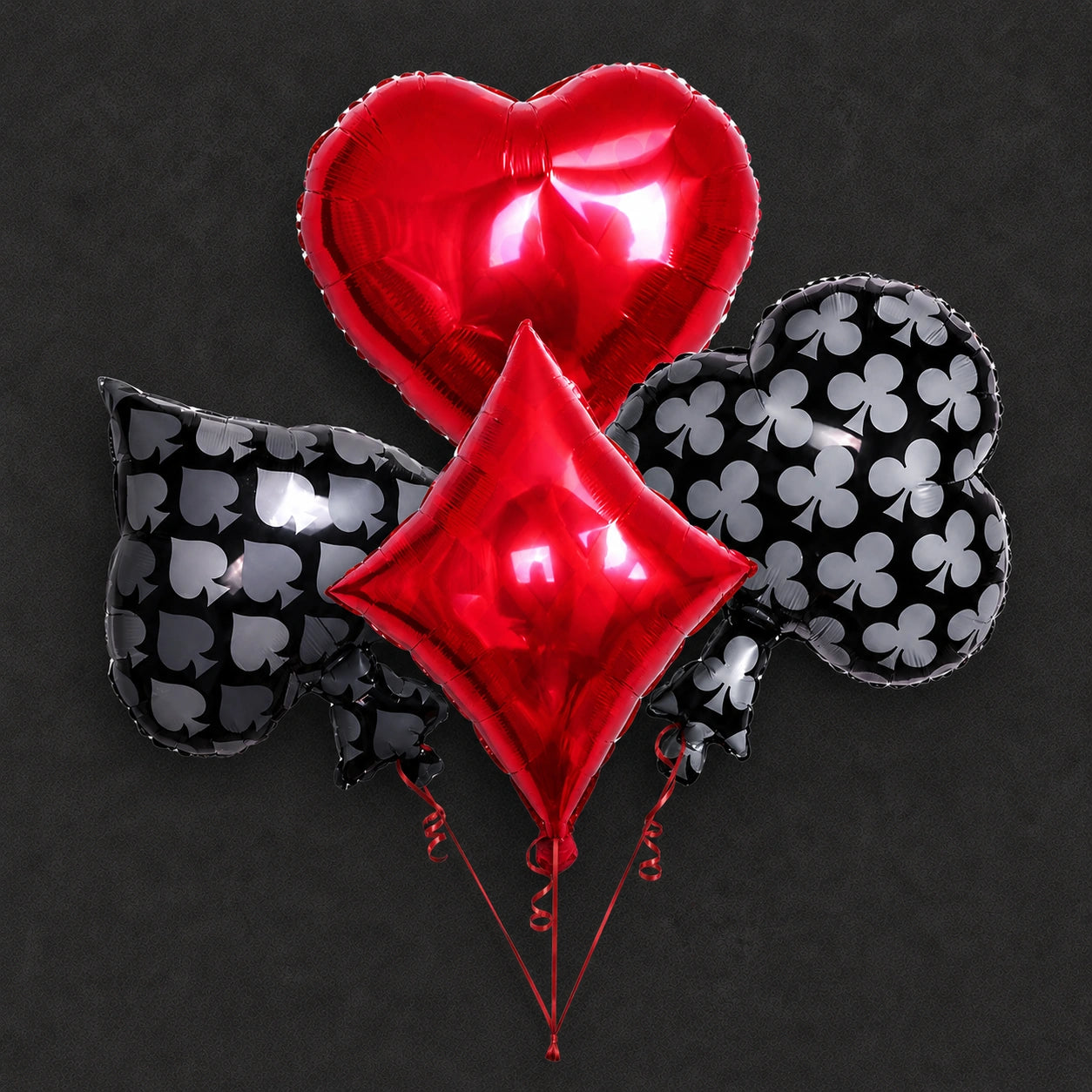 A set of metallic foil balloons shaped like a red heart, a red diamond, and black playing card suits with white symbols, arranged against a dark textured background.