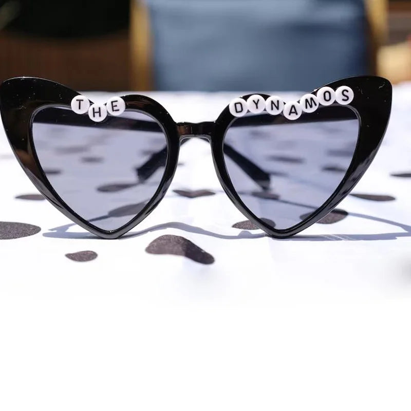 Heart-shaped sunglasses with 'The Dynamos' on a reflective surface