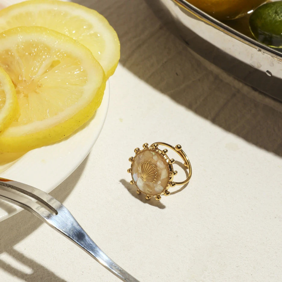 Gold ring with shell design on a white surface with lemon slices and a fork.