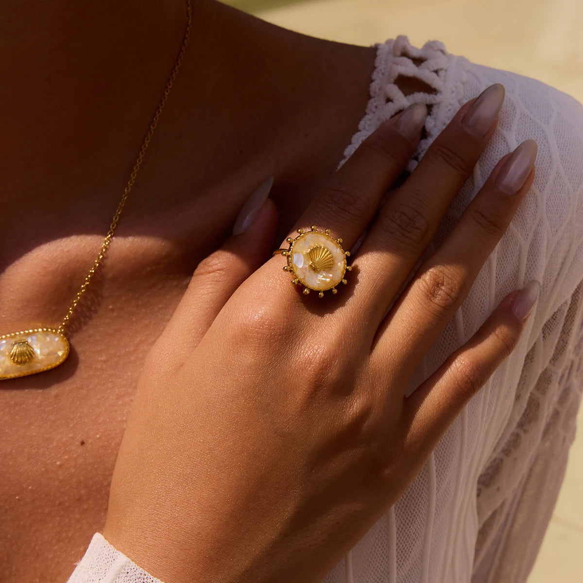 Close-up of a hand wearing a gold ring with a floral design, against a neutral background.