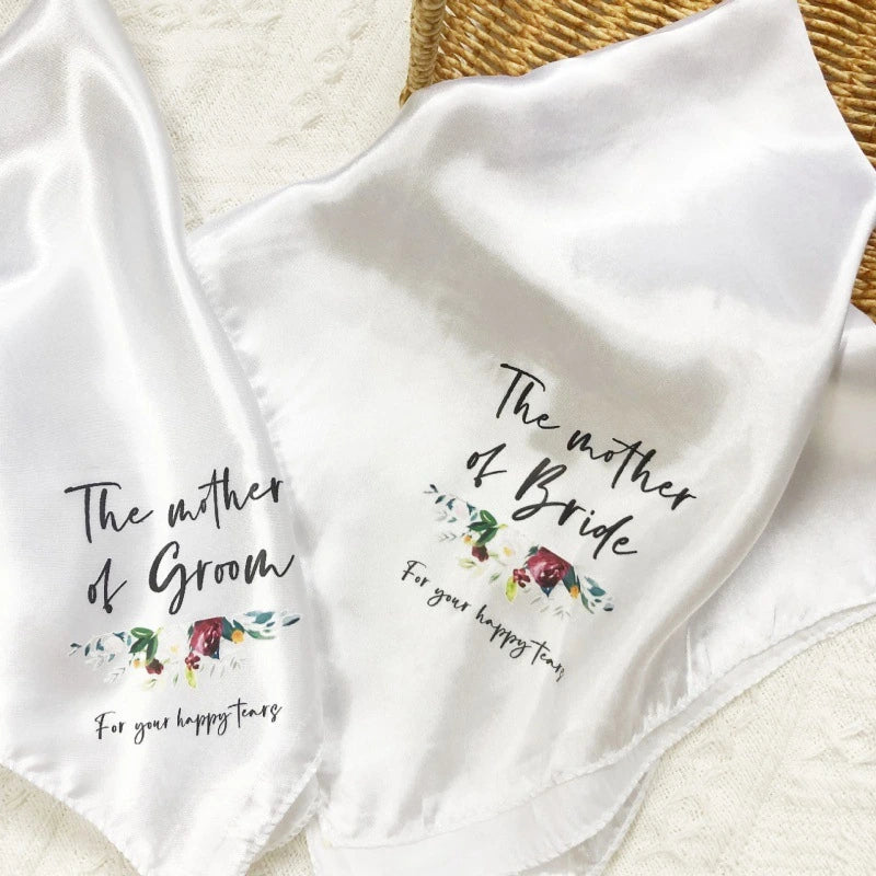 Two white satin handkerchiefs with personalized text and floral designs on a textured surface.