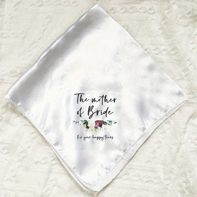 A white satin baby gift scarf with 'The mother of Bride' and 'For your happy tears' printed on it, laid flat on a textured cream fabric background.