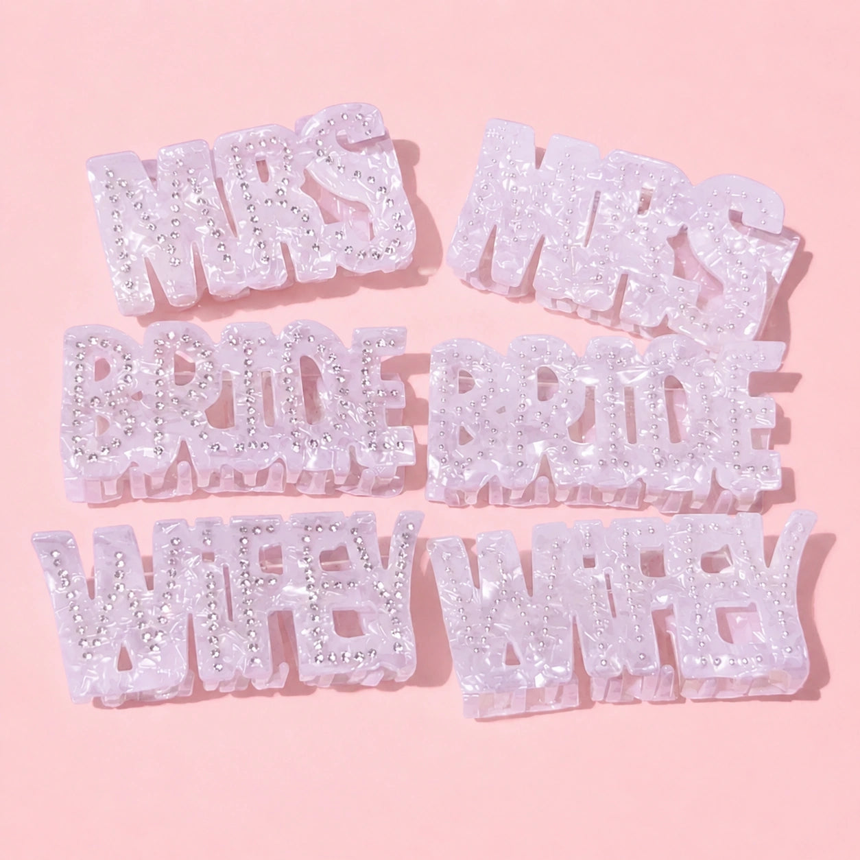 Set of glittery letter pieces spelling 'MRS.', 'BRIDE', 'WIFE' on a pink background