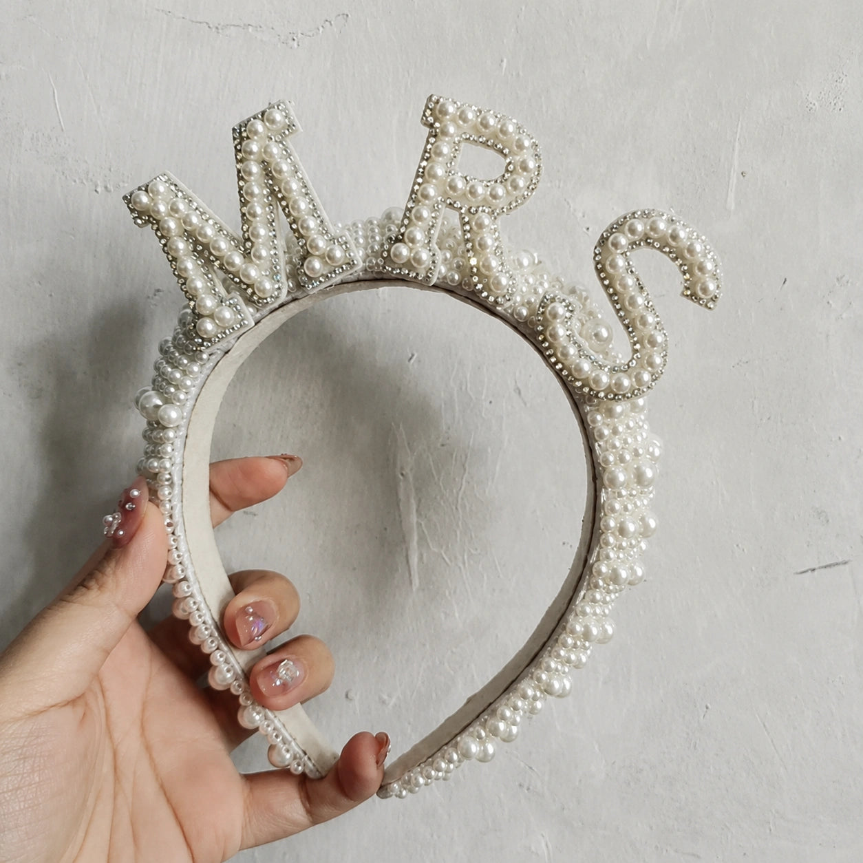 Pearl embellished “MRS” bridal headband held against a neutral textured background.