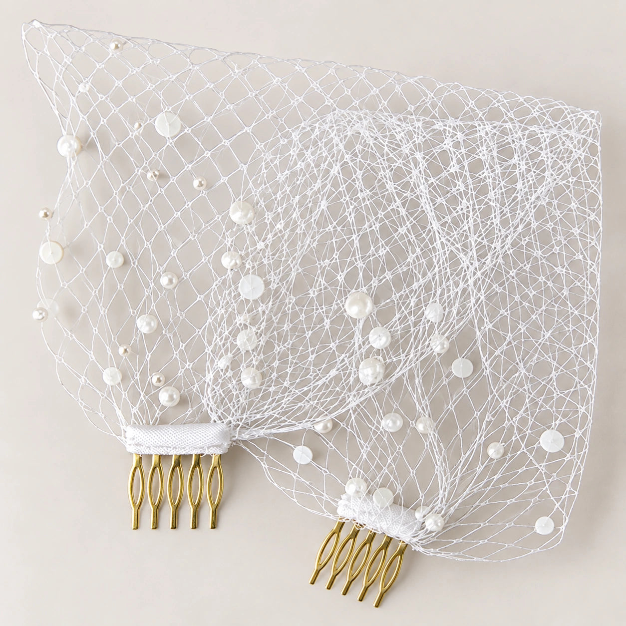 White bridal veil with pearl embellishments and two gold-tone hair combs, displayed flat against a light beige background.