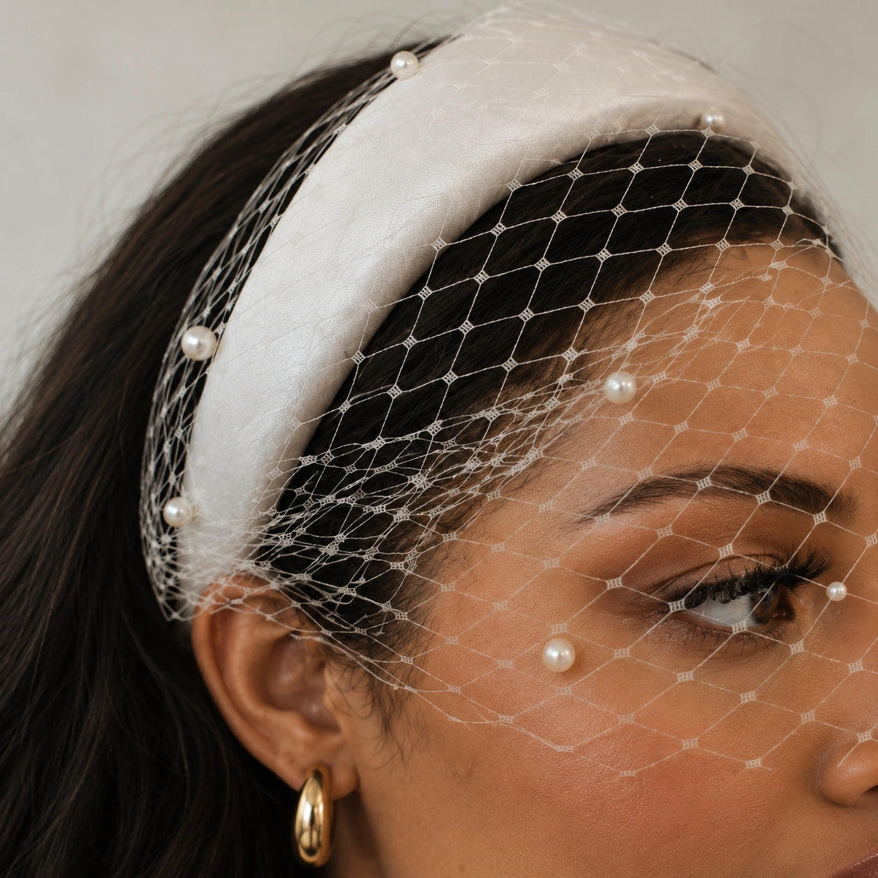 A close-up of a woman wearing a white fabric headband with a white net veil decorated with small pearl-like beads.