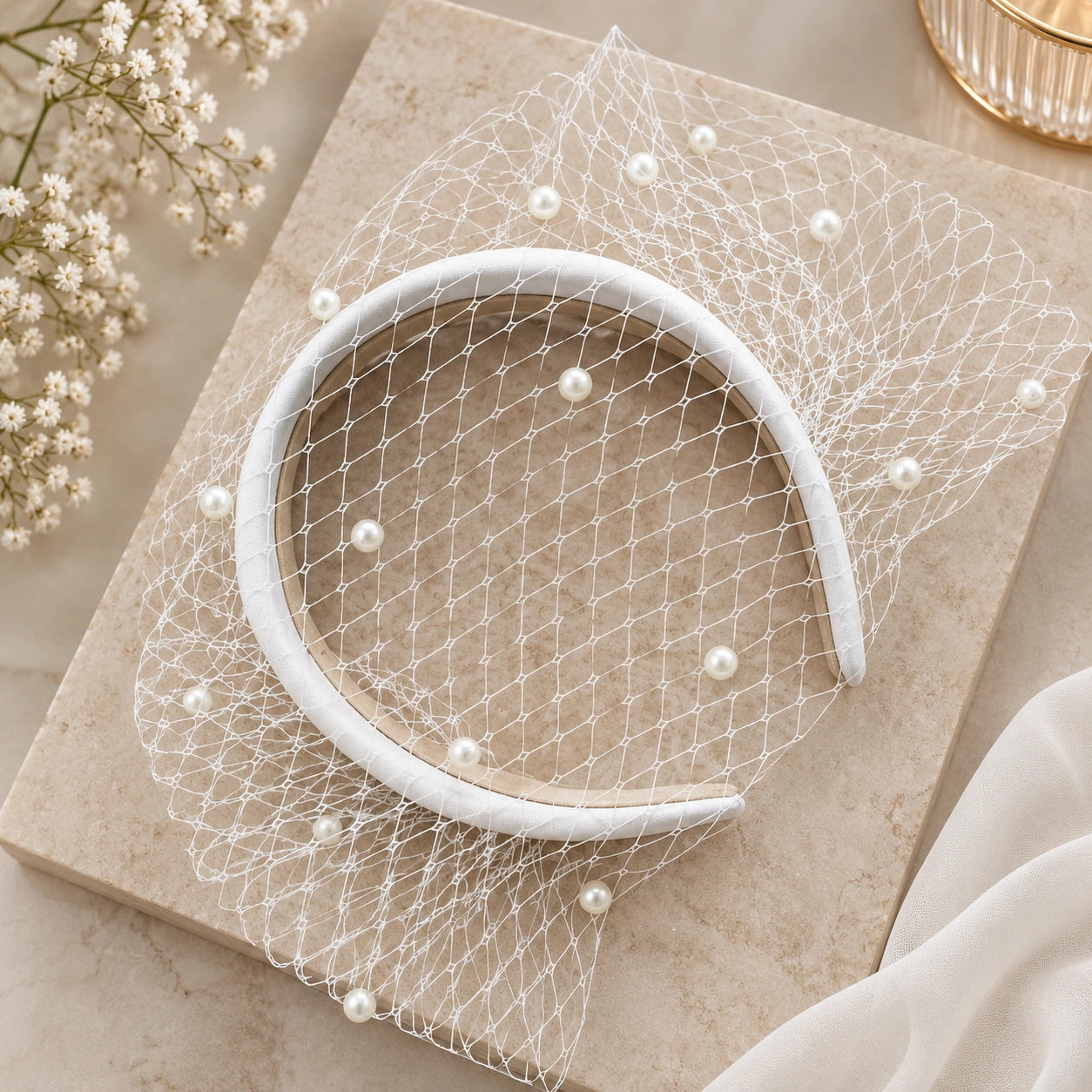 A white bridal headband with a delicate white net veil decorated with small pearl-like beads.