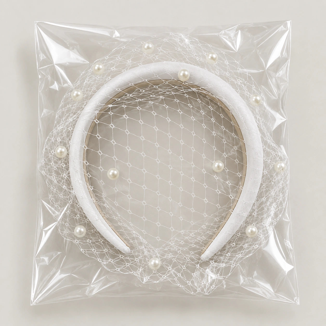 A white velvet bridal headband with a delicate white tulle net veil and scattered faux pearl beads, packaged inside a clear plastic bag.