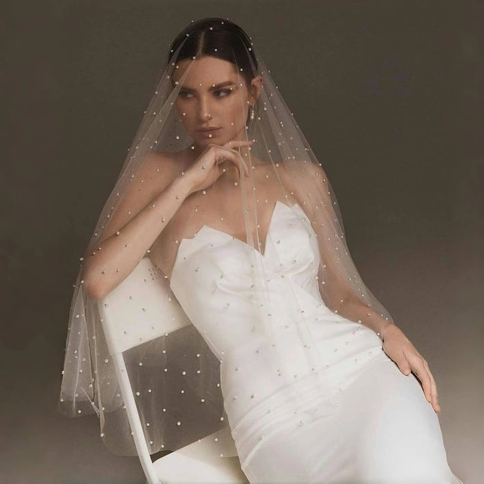 Bride wearing the Pearl Dream Bridal Veil with soft pearl-dotted tulle while seated in a white bridal dress.