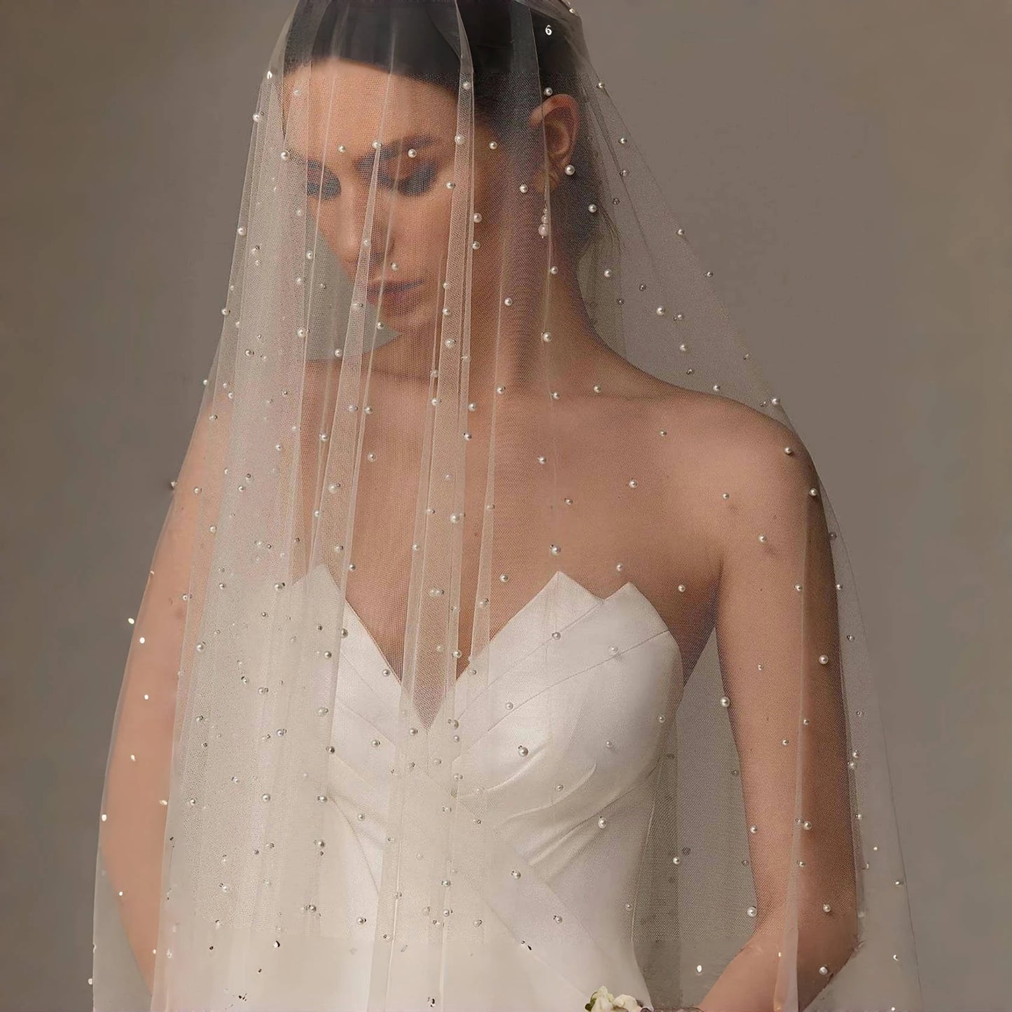 Standing bride wearing a pearl-dotted bridal veil with soft layered tulle and a white wedding dress.