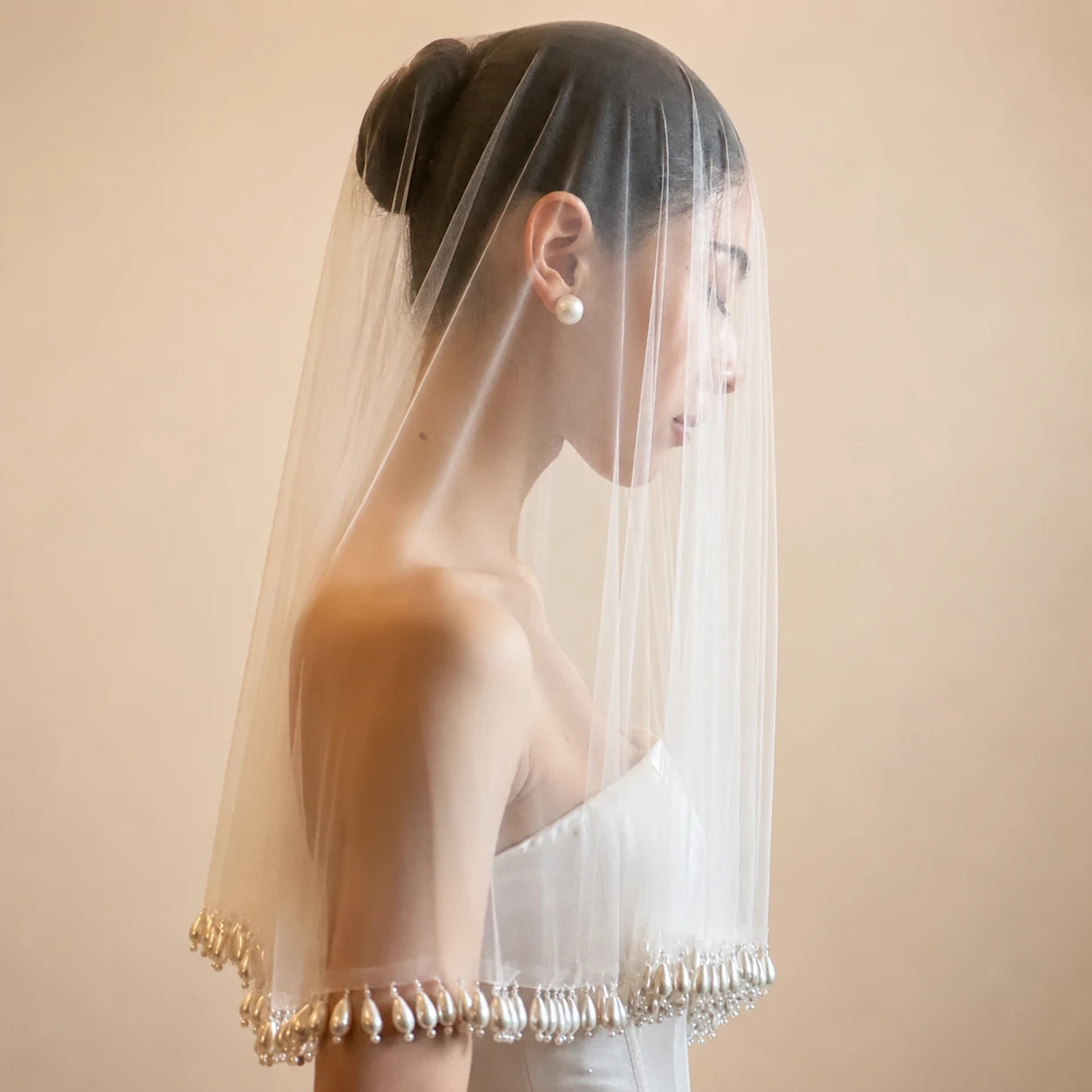 Woman wearing a white wedding dress with a veil and pearl details on a beige background