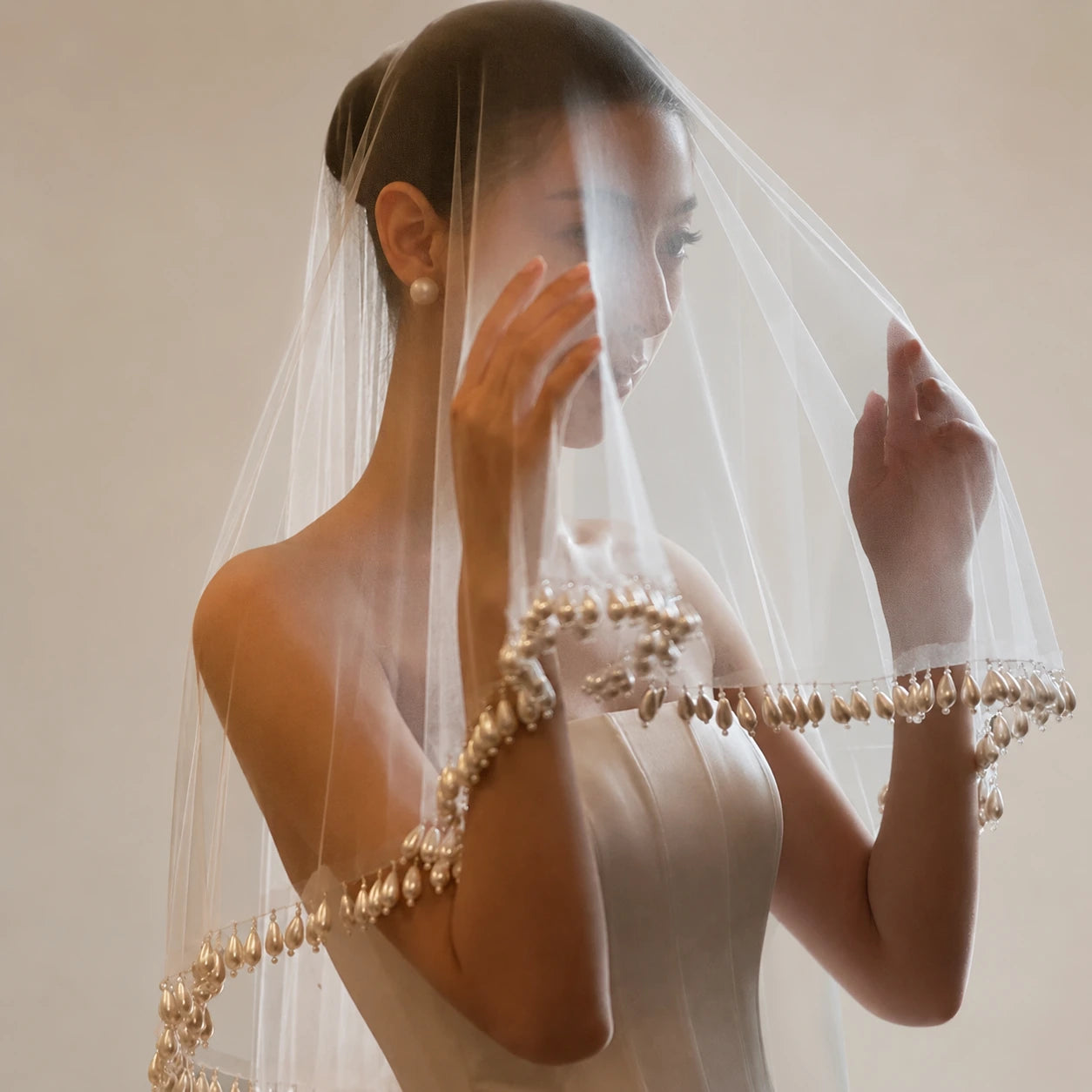 Woman wearing a white wedding dress with a decorative veil against a neutral background