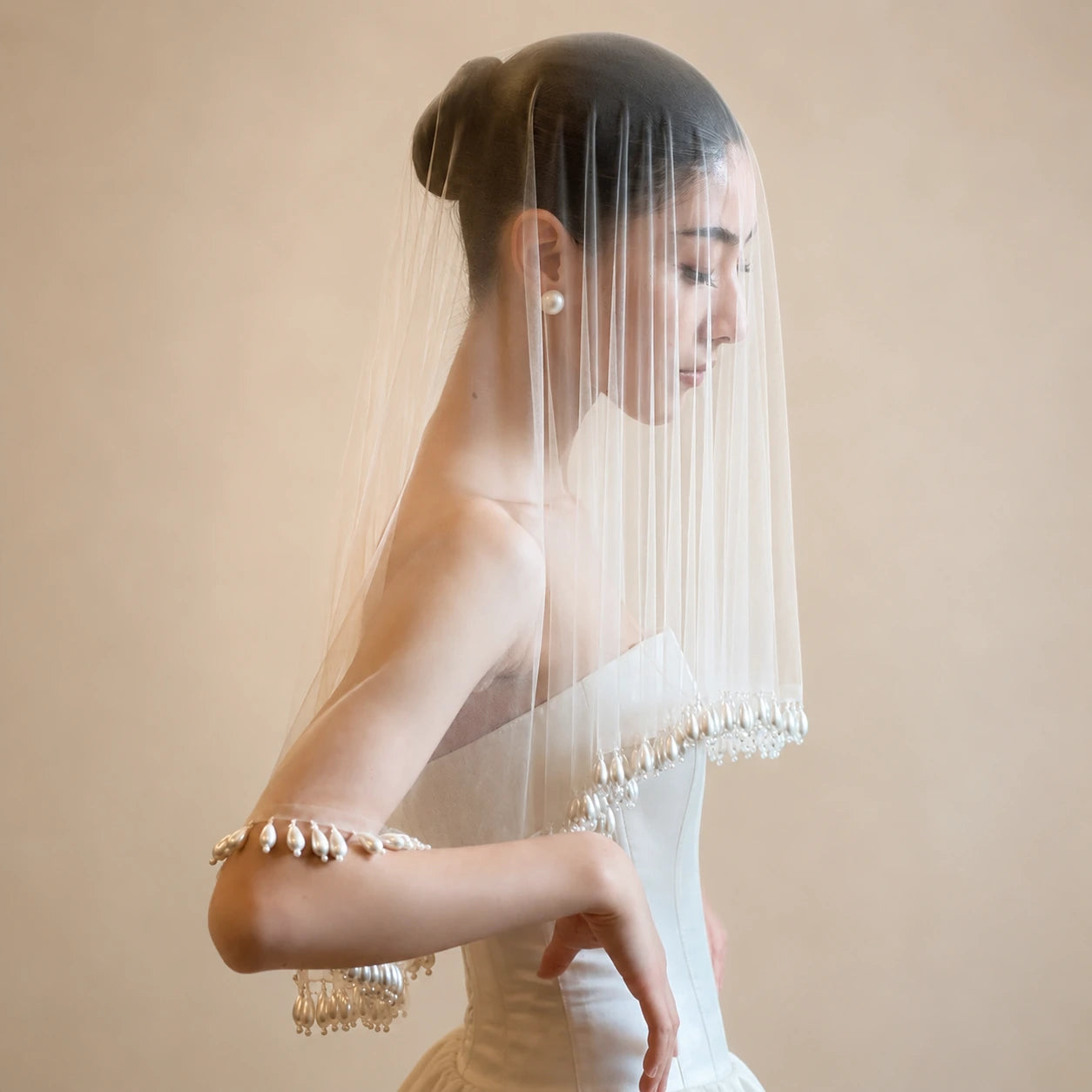 Woman wearing a white wedding dress with a veil against a beige background