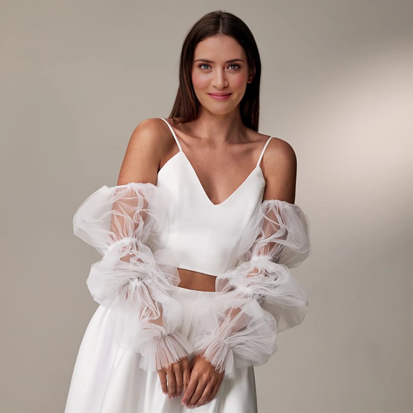 Woman wearing a white dress with sheer sleeves against a neutral background