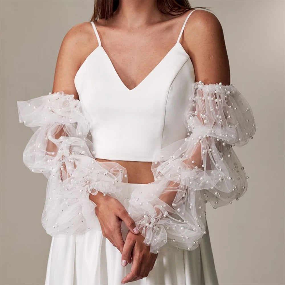 White top with sheer sleeves and pearl details on a neutral background