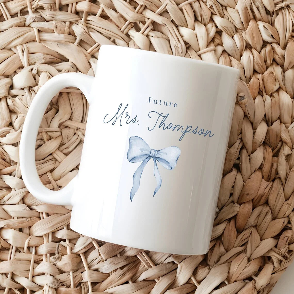 White mug with 'Future Mrs. Thompson' text and blue bow graphic on a woven mat
