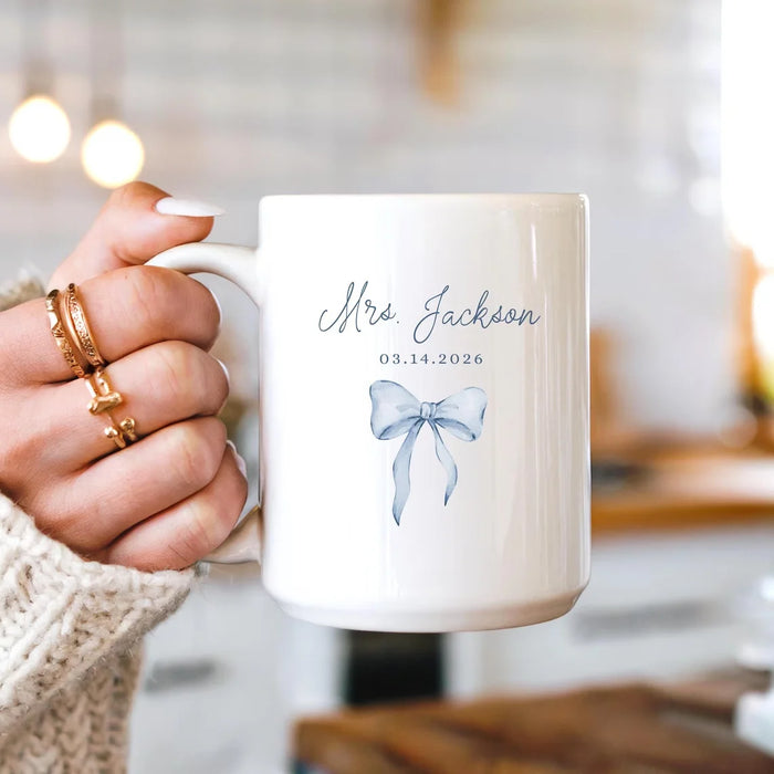 White mug with personalized text and bow design, held by a hand.