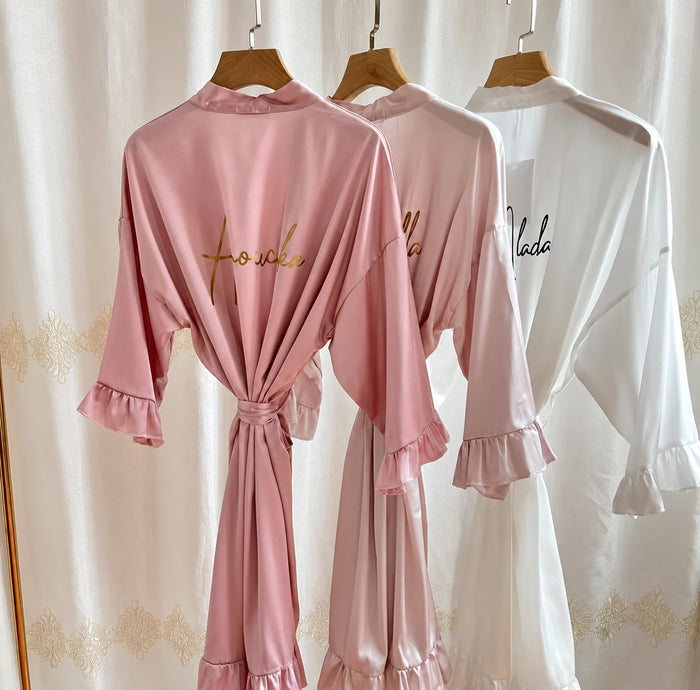 Pink satin pajama set with 'Foulee' branding on hangers against a white curtain background.