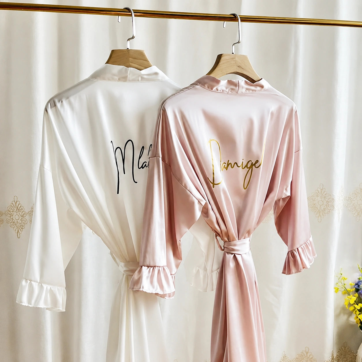 Two satin robes, one white and one pink, hanging on a rod with decorative elements.