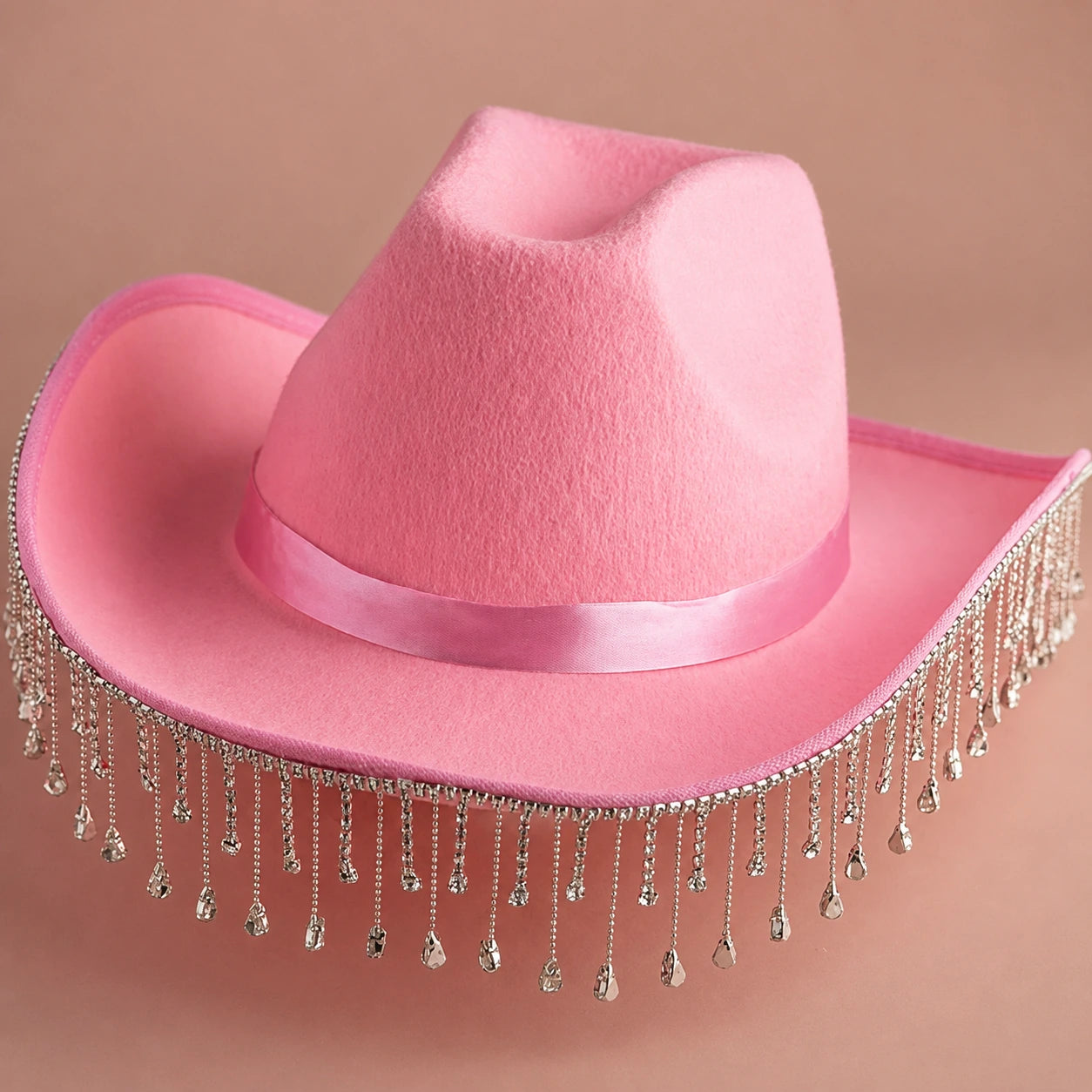 Pink cowboy hat with decorative tassels on a beige background