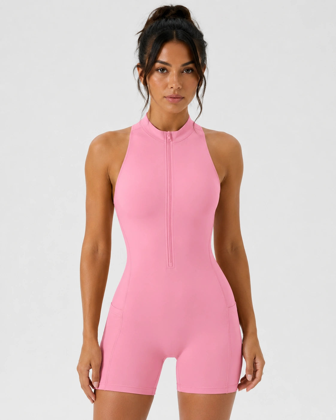 A woman modeling a bright pink sleeveless one-piece jumpsuit with a high mock neck and a front zipper, set against a plain light gray studio background.