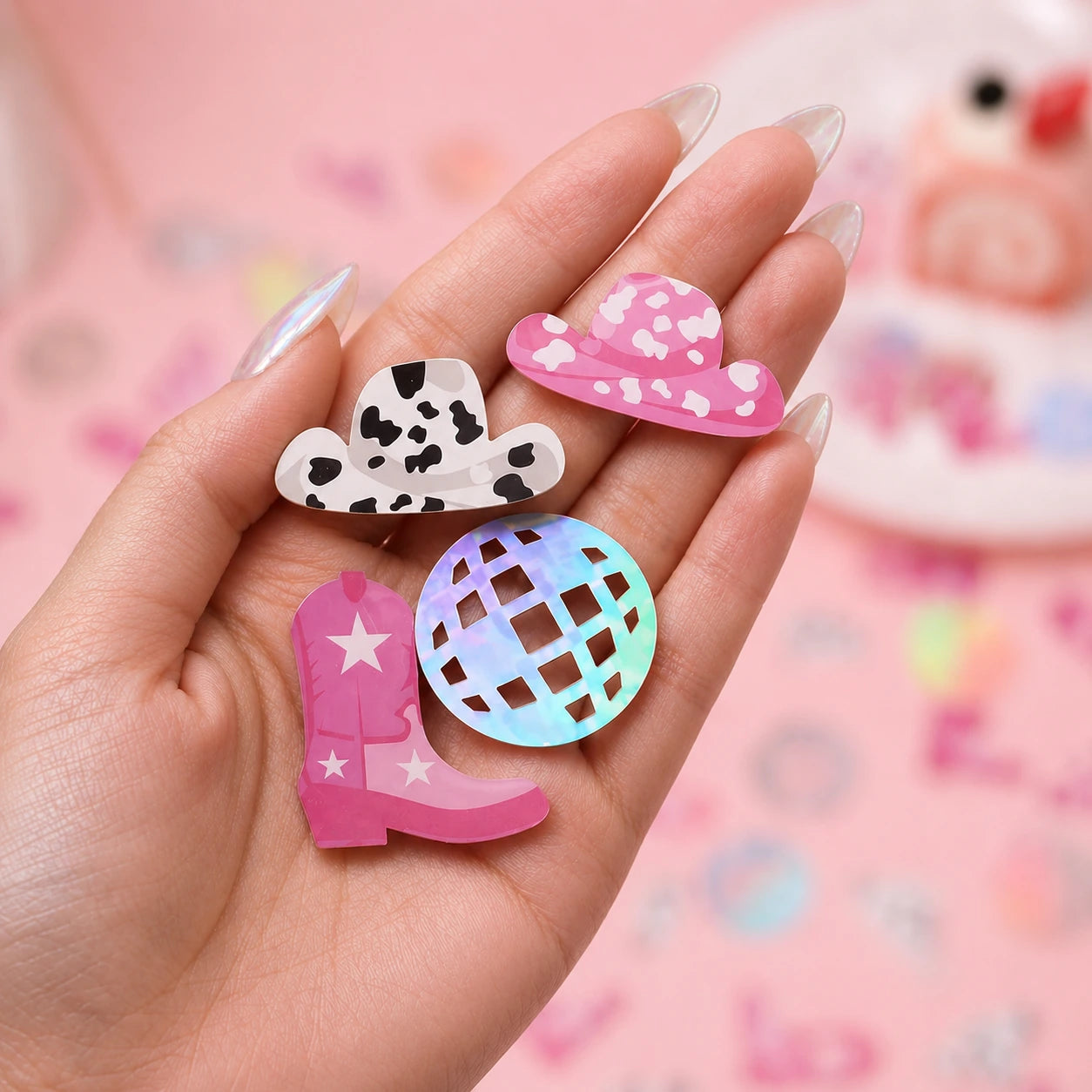 Hand with iridescent nails holding cowgirl hat, boot, and disco ball confetti on pink background