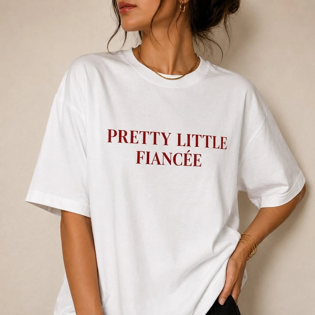 White t-shirt with 'PRETTY LITTLE FIANCéE' text worn by a person on a beige background