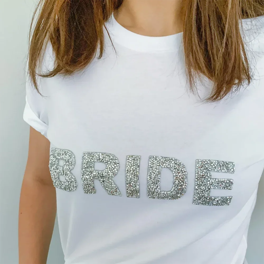 Close-up of a white bride t-shirt with silver rhinestone lettering, styled for a bridal shower, bachelorette party, or getting ready outfit from The Hen Planner.