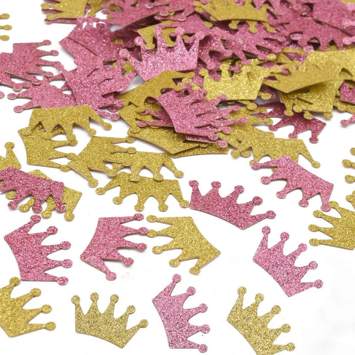 Pink and gold glittery crown-shaped confetti on a white background