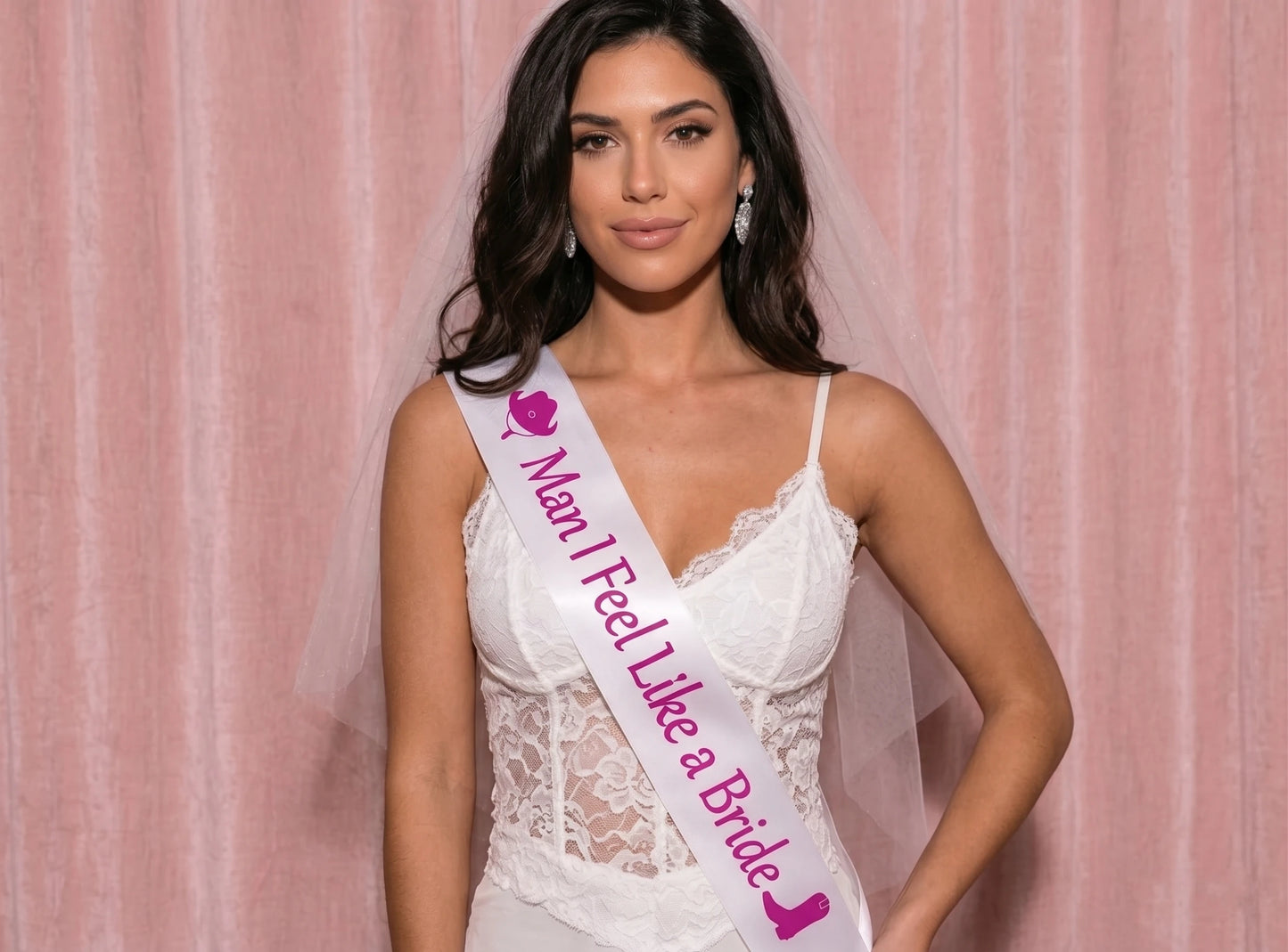 Woman wearing a white lace dress with a sash that reads 'Man I Feel Like a Bride' against a pink background.