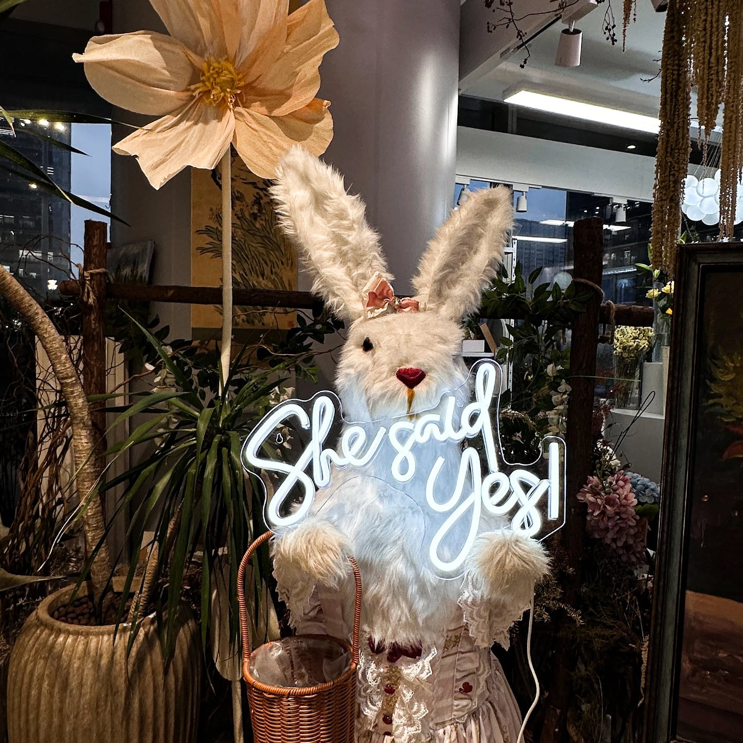 Decorative bunny with 'She said Yes!' neon sign in a plant-filled room