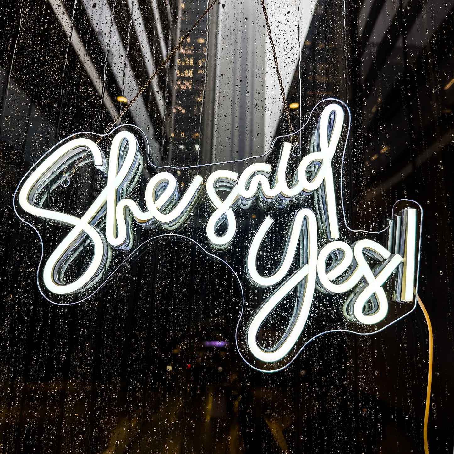Neon sign with 'She said Yes' on a rainy window with cityscape background