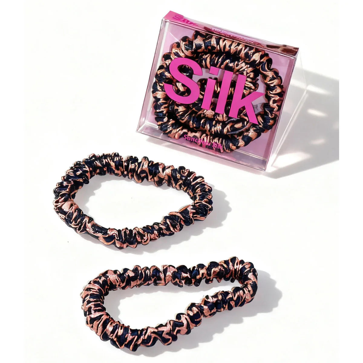 Set of leopard print scrunchies with a pink 'SILK' container on a white background