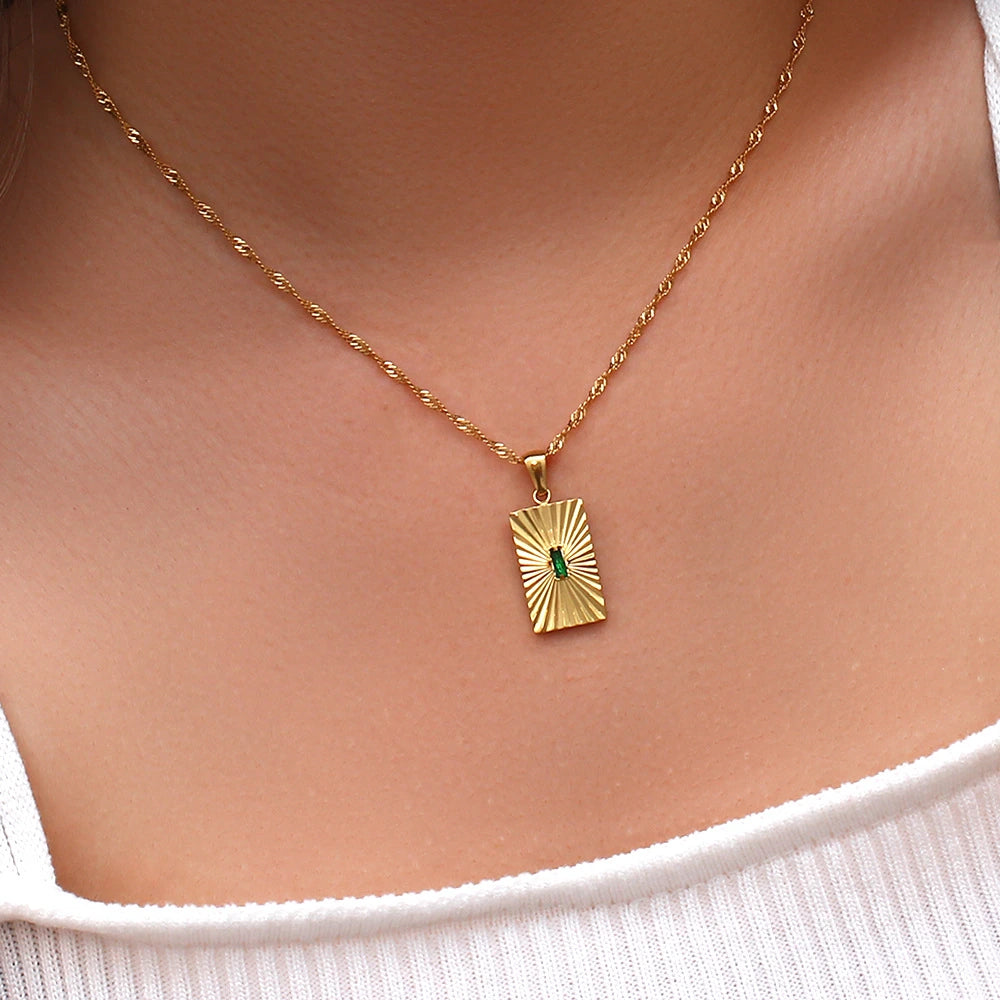 Gold necklace with a green gemstone pendant on a person wearing a white top.