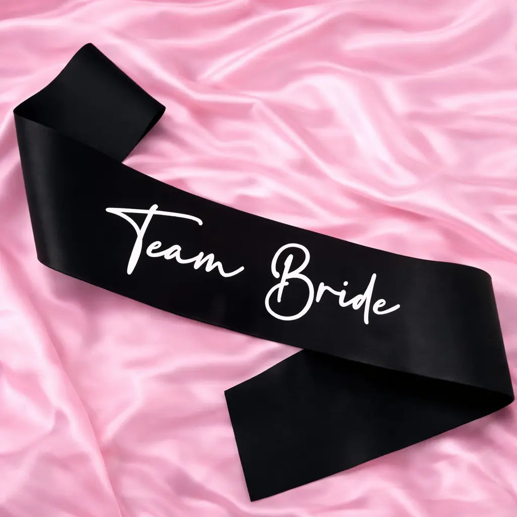 Black sash with 'Team Bride' text on a pink fabric background