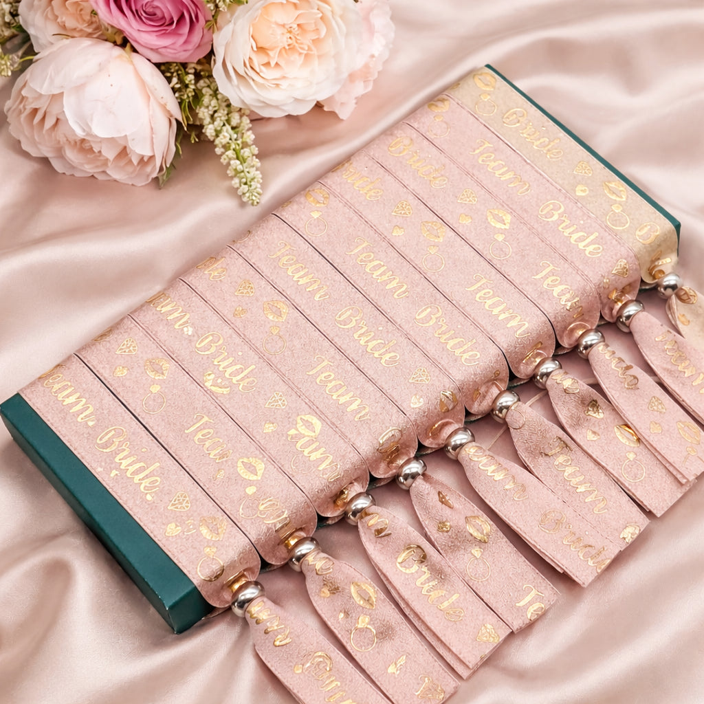 Set of pink ribbons with gold text on a satin surface, accompanied by pink flowers.
