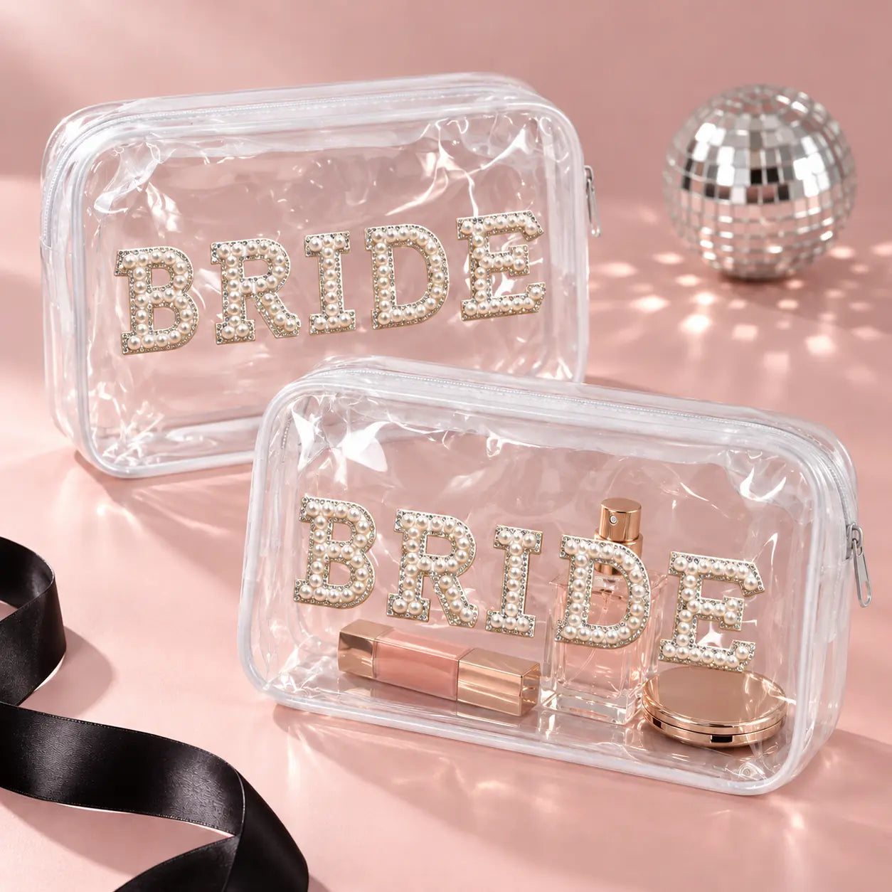 Two clear zippered cosmetic bags with 'BRIDE' lettering in rhinestones, styled on a pink background with a disco ball and black ribbon.