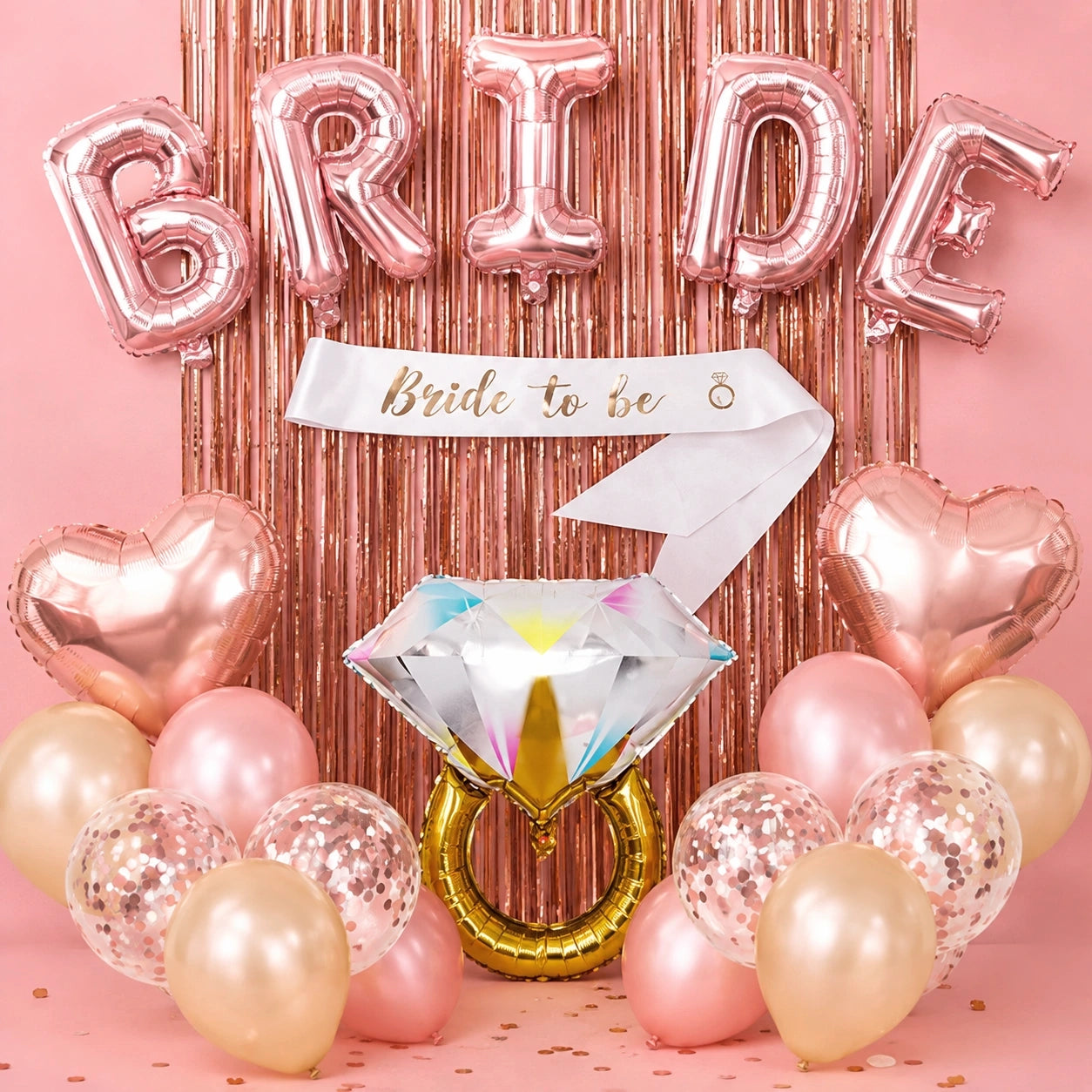 Bride-to-be party balloon set with metallic rose gold foil balloons spelling BRIDE, a white sash reading Bride to be, heart-shaped balloons, a large diamond ring balloon, and assorted pink, champagne, and rose gold balloons against a pink tinsel backdrop.