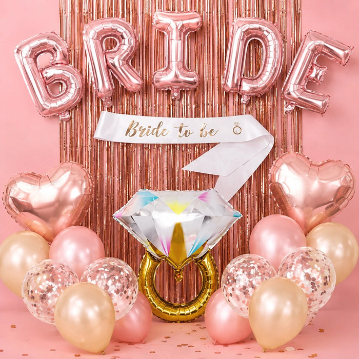 Bride-to-be party balloon set with metallic rose gold foil balloons spelling BRIDE, a white sash reading Bride to be, heart-shaped balloons, a large diamond ring balloon, and assorted pink, champagne, and rose gold balloons against a pink tinsel backdrop.