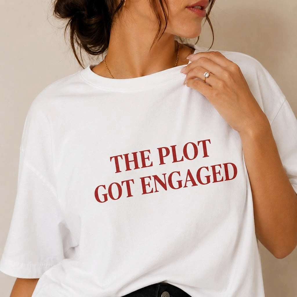 Person wearing a white t-shirt with red text 'THE PLOT GOT ENGAGED' on a neutral background