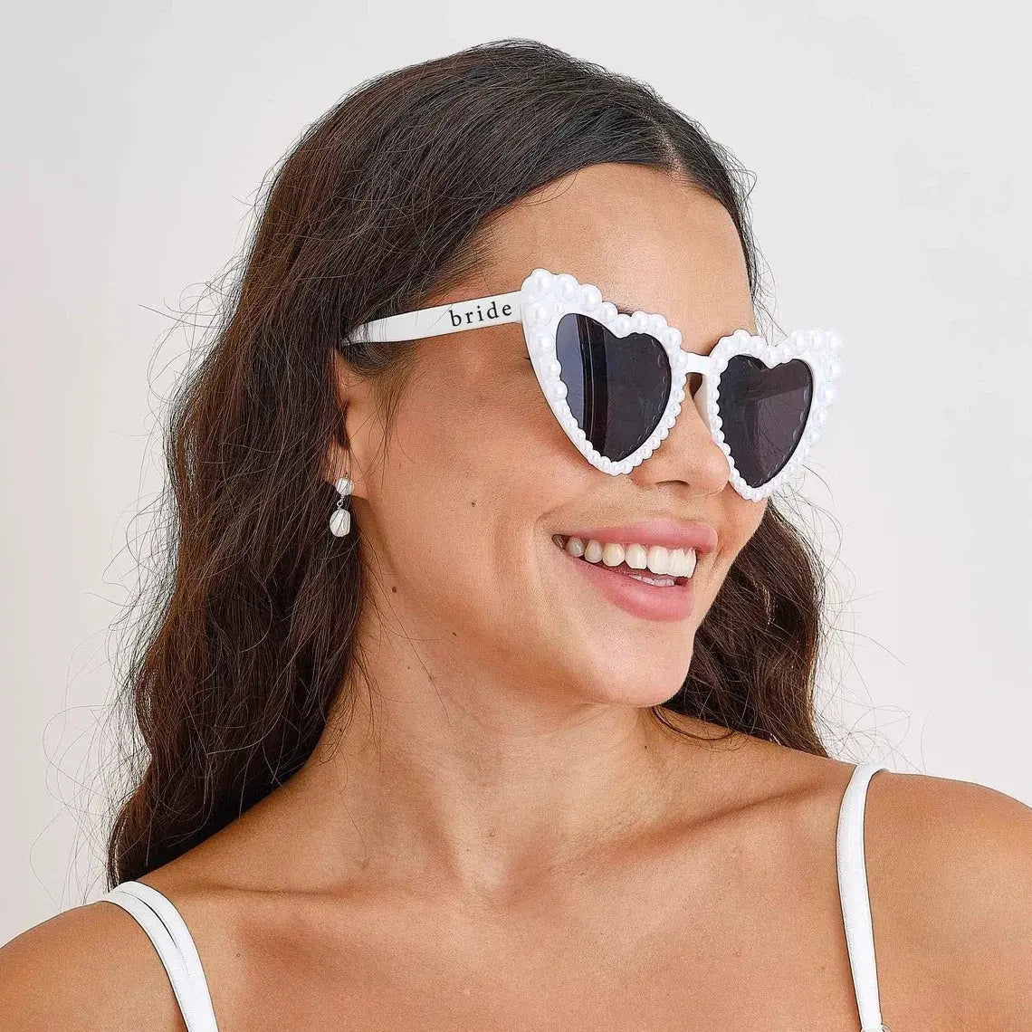 Bride wearing white pearl heart sunglasses with bride lettering, styled for a bachelorette party look from The Hen Planner.