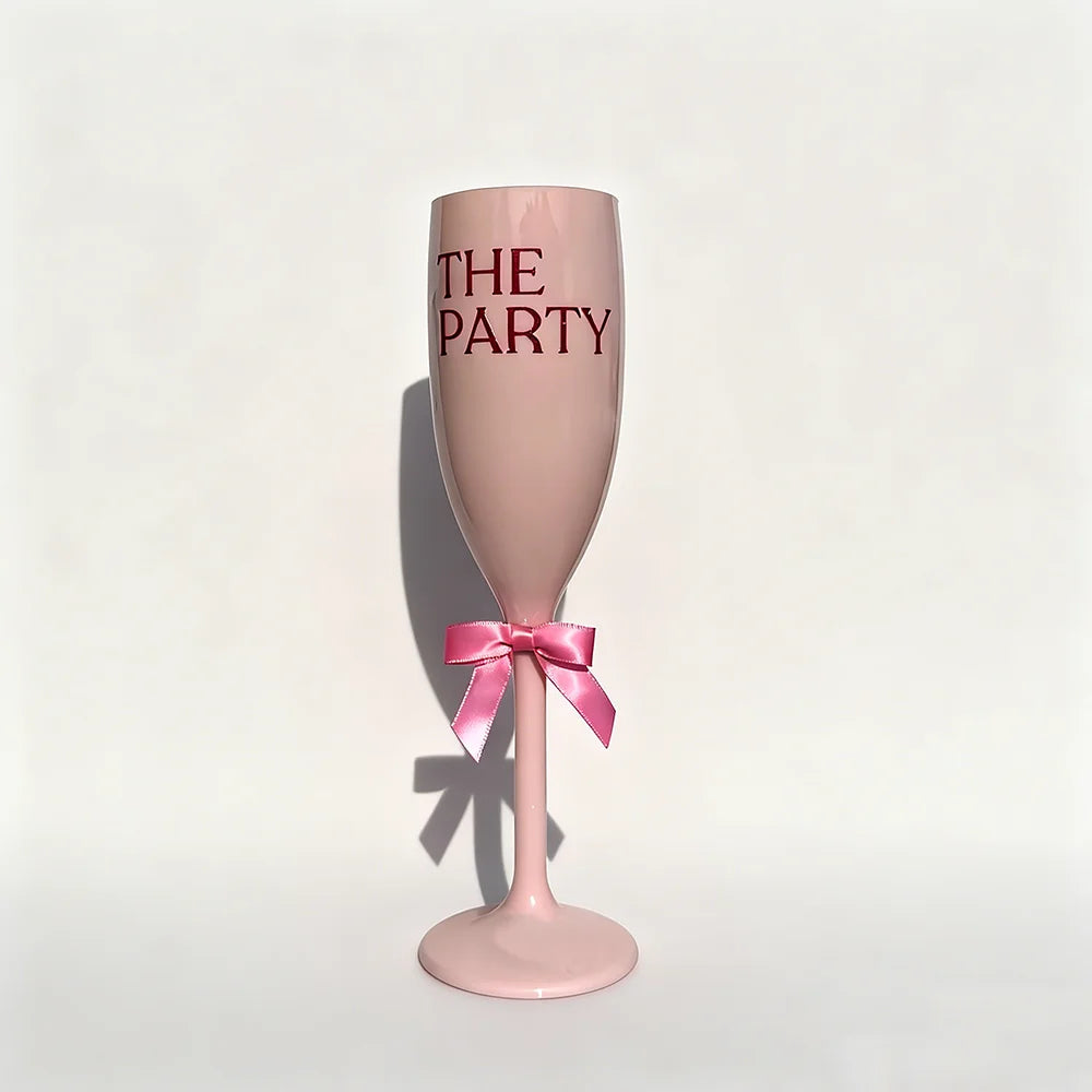 Pink champagne flute with 'THE PARTY' text and a pink bow on a light gray background