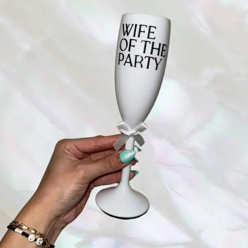 White champagne flute with 'Wife of the Party' text held by a hand against a light background