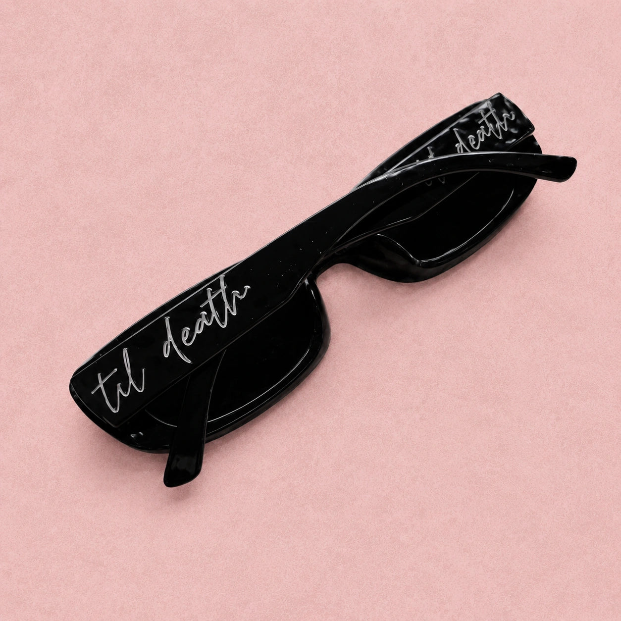 Black sunglasses with 'til death' text on a pink background