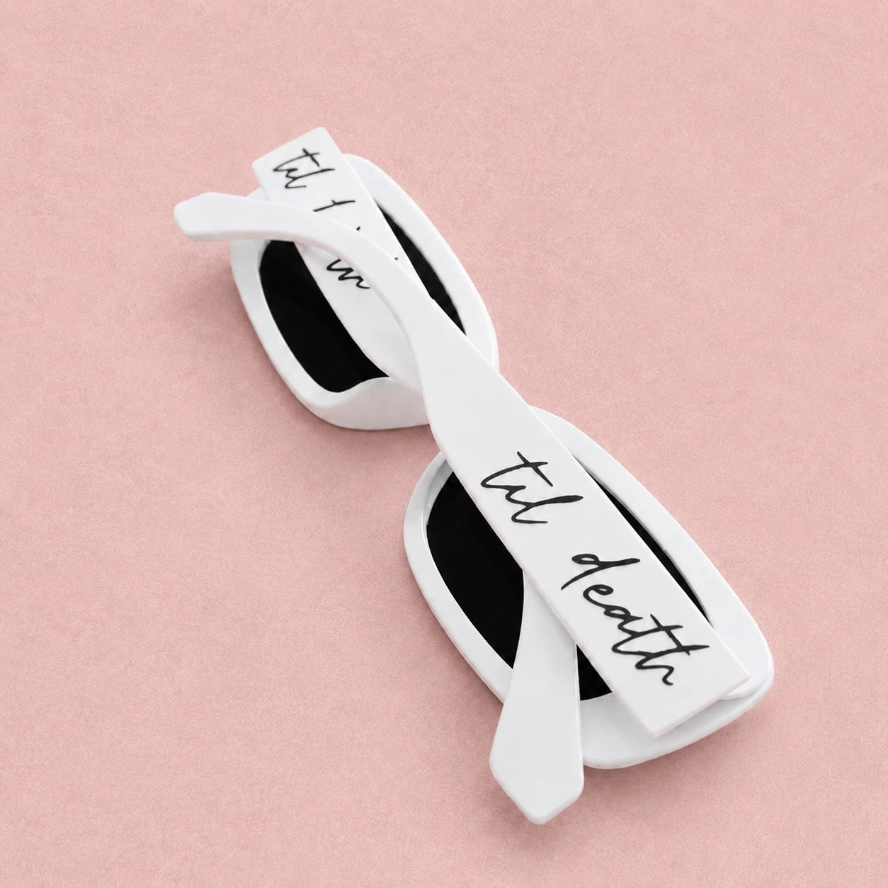 White sunglasses with 'til death' text on a pink background